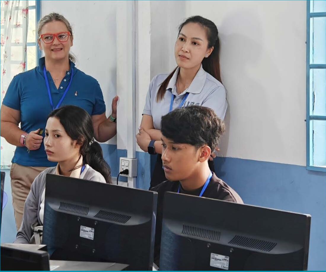 Two facilitators standing behind students working at their screens during the workshop